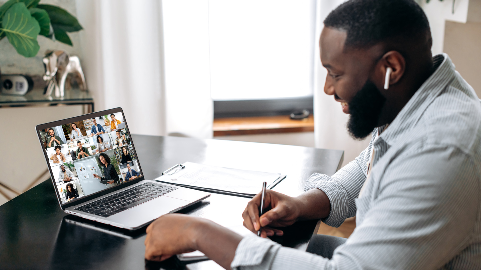 Man taking notes while watching a virtual training on a laptop